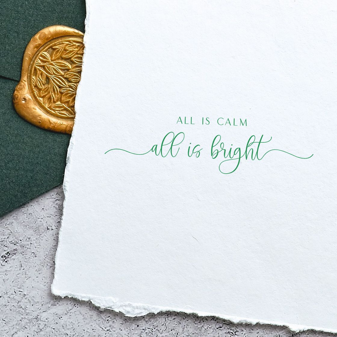 Gold wax seal with leaf motif beside white handmade paper stamped in green, reading all is calm, all is bright.