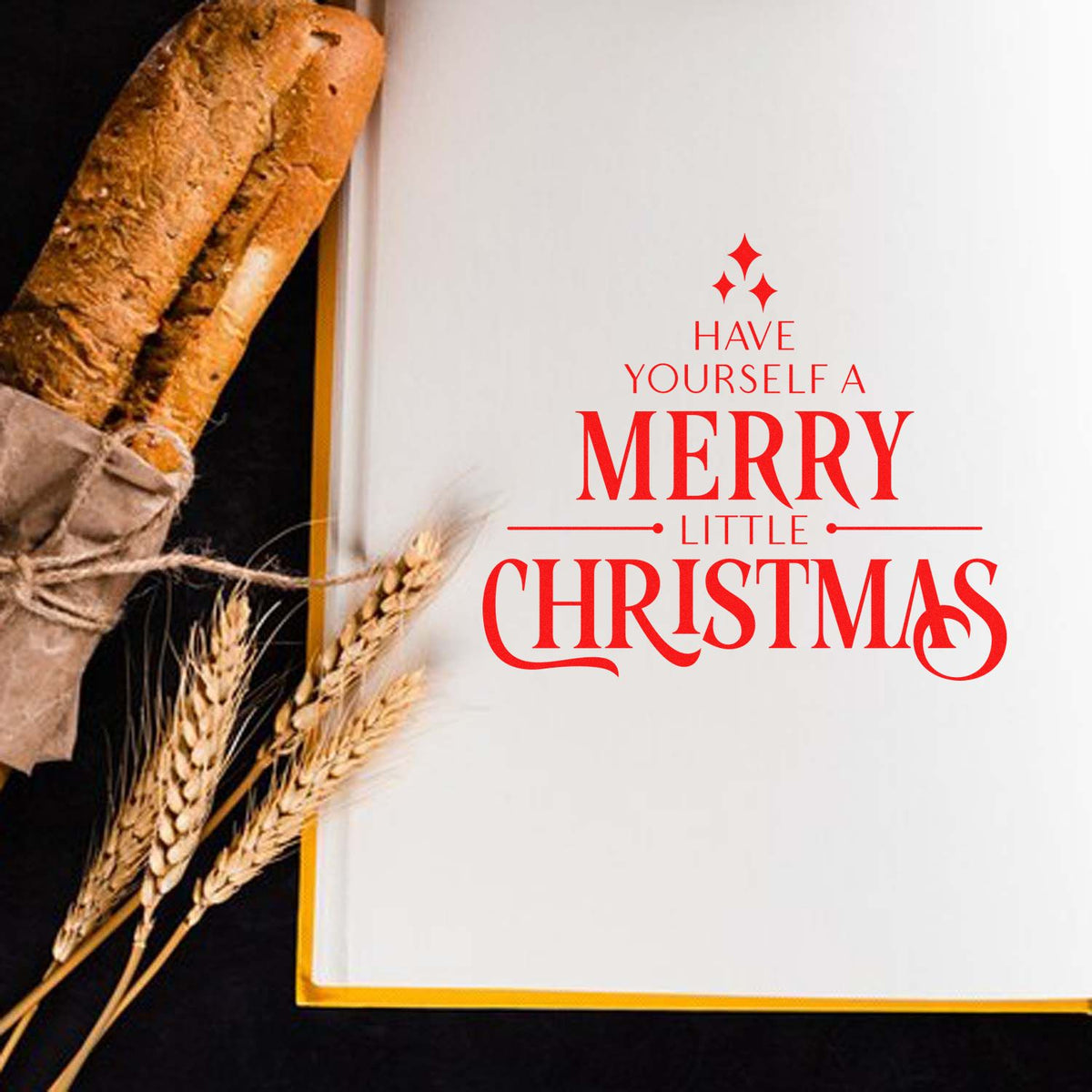 Red Christmas stamp and seal on white paper reading Have Yourself a Merry Little Christmas, beside rustic bread and wheat.
