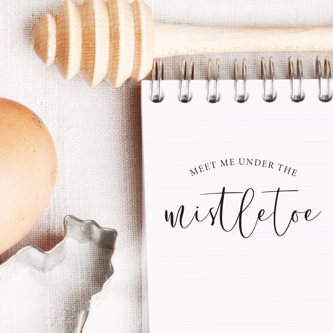 Wooden stamp and seal products, honey-toned and silver, beside a white spiral notebook reading Meet me under the mistletoe.