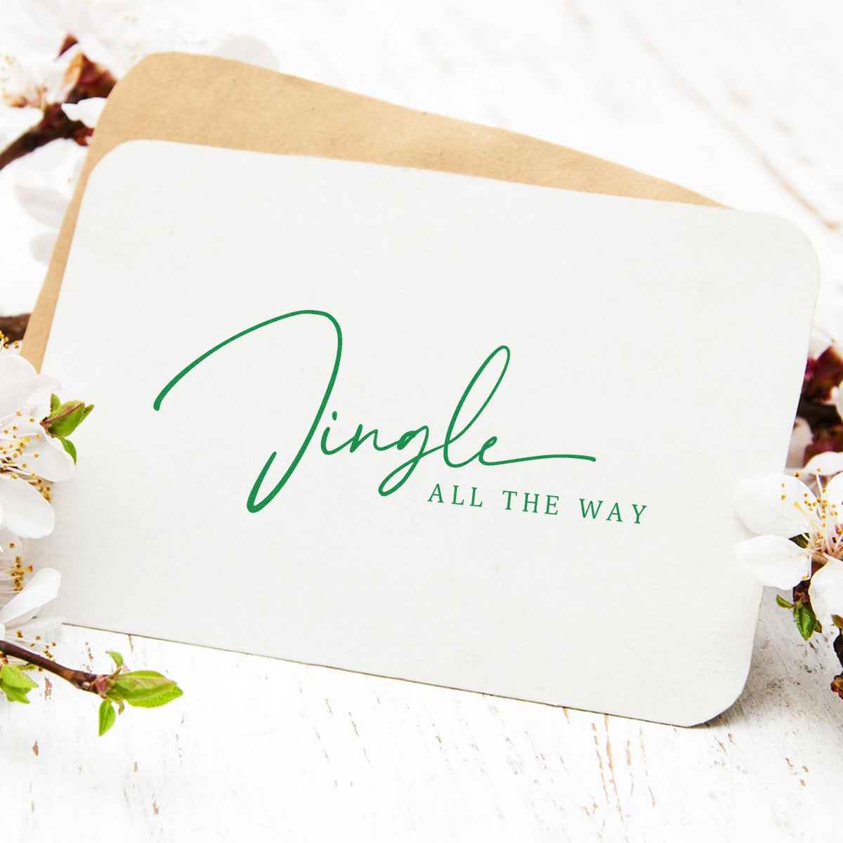White custom stamp and seal cards with green Jingle All the Way lettering, tan envelope, and spring blossoms.