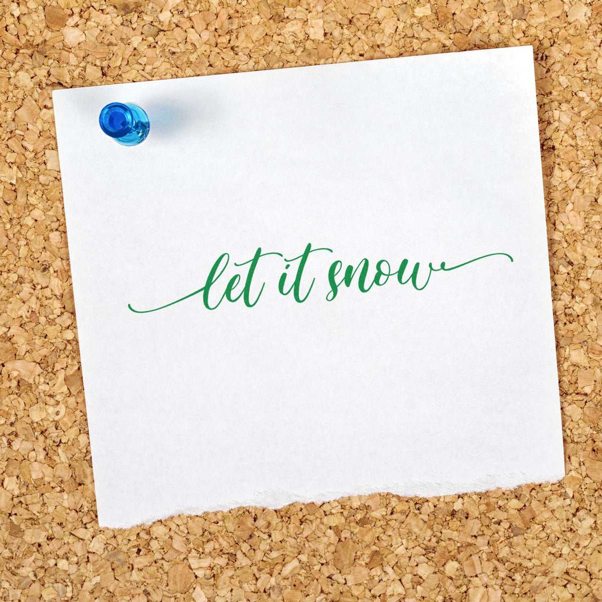 White cardstock with green let it snow script and a blue seal stamp pin on a corkboard background.