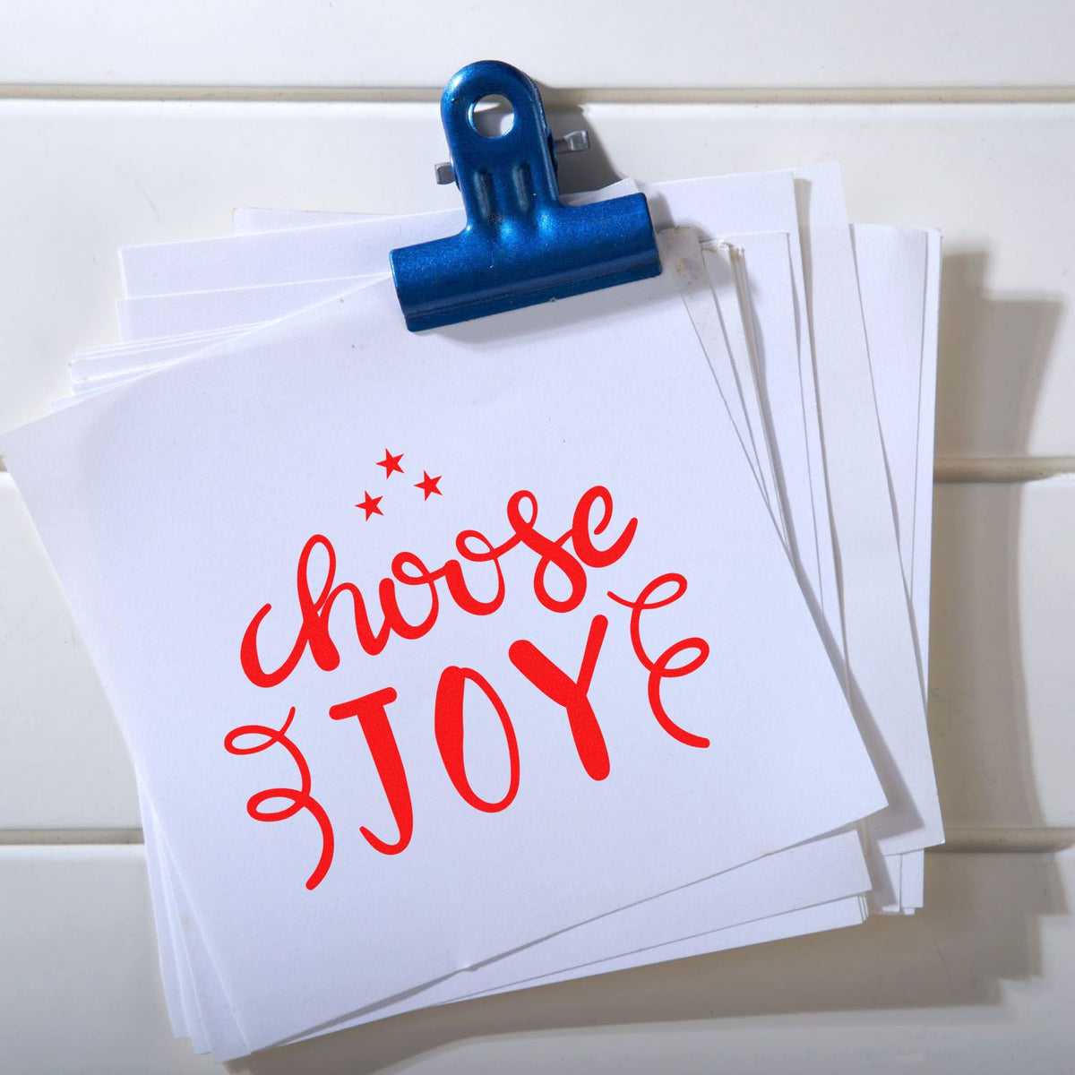Blue binder clip holding stack of white stamp and seal cards with red choose JOY lettering