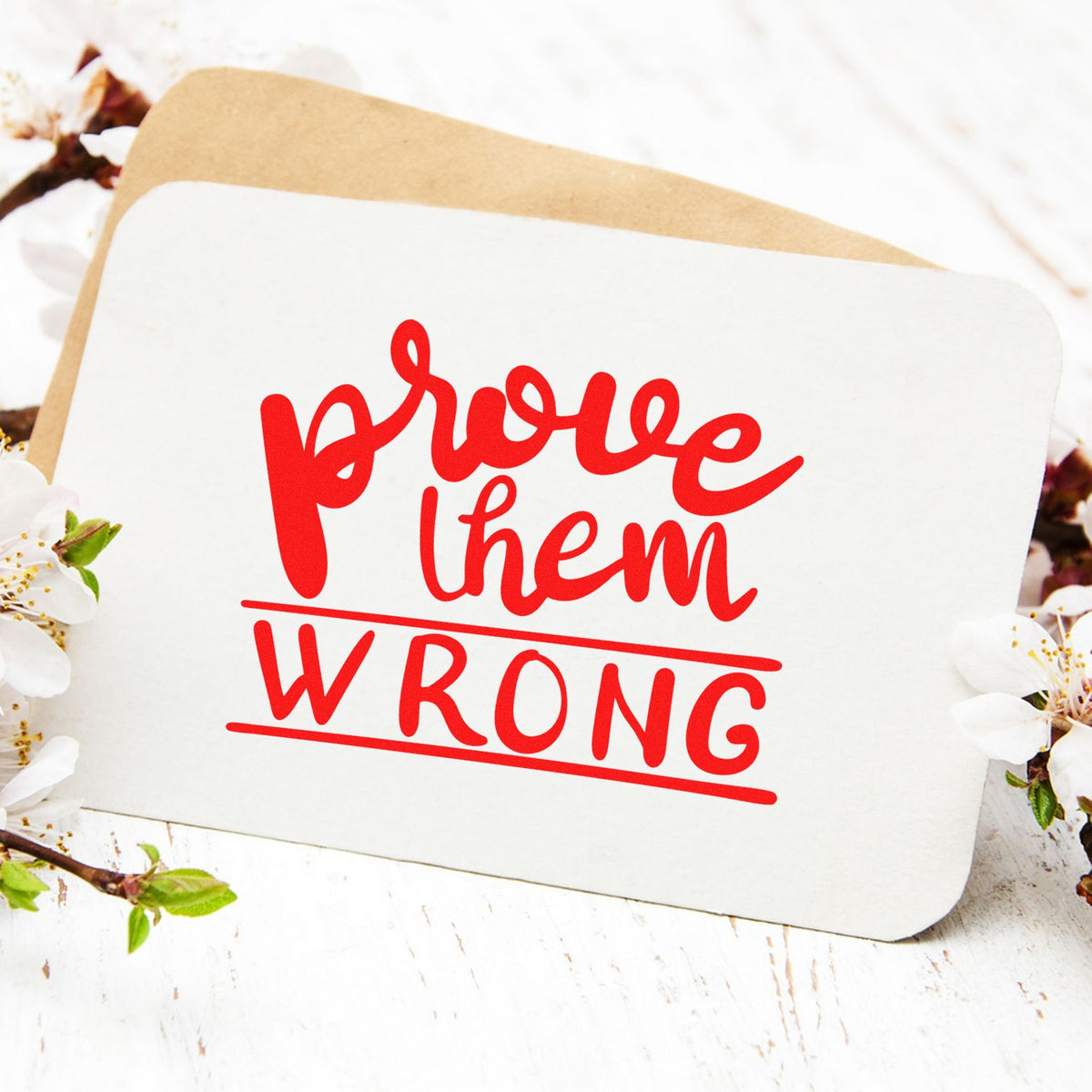 Red prove them wrong stamp and seal on white card with tan backing and floral accents.