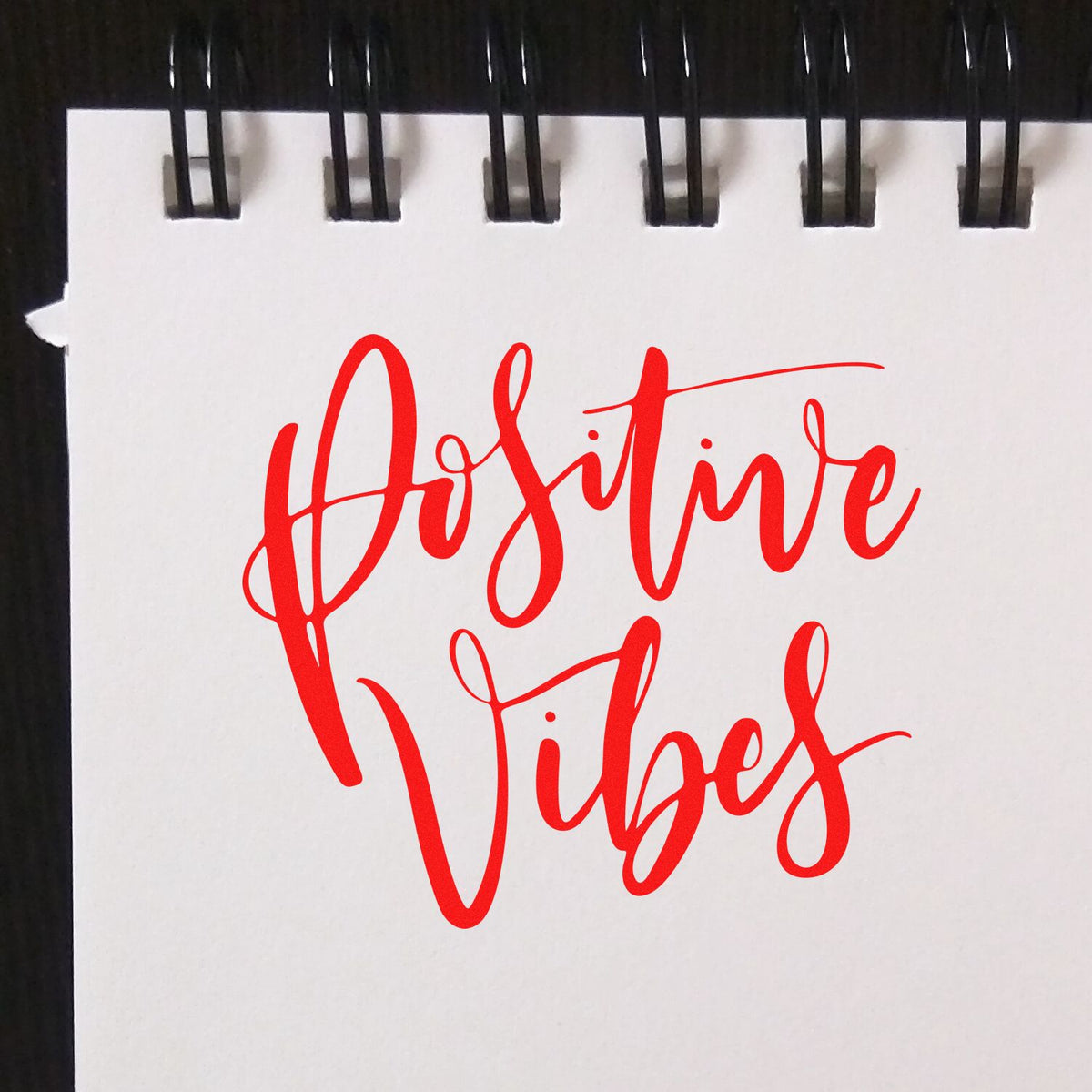 Red Positive Vibes script stamp on white spiral notepad, bold red calligraphy seal design.