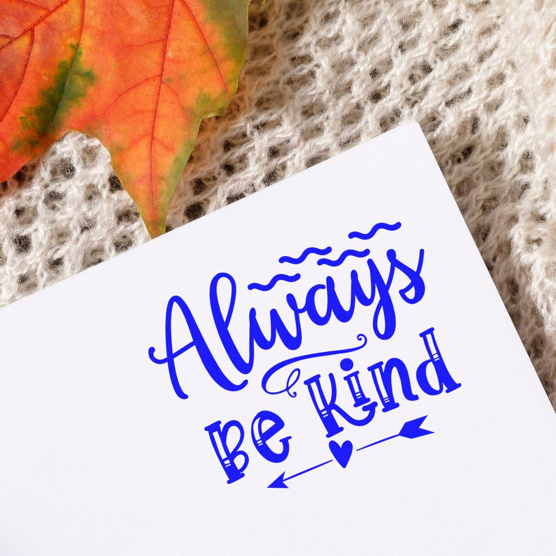 Blue Always Be Kind stamp and seal on white card with heart, arrows, and autumn leaf on knit fabric.