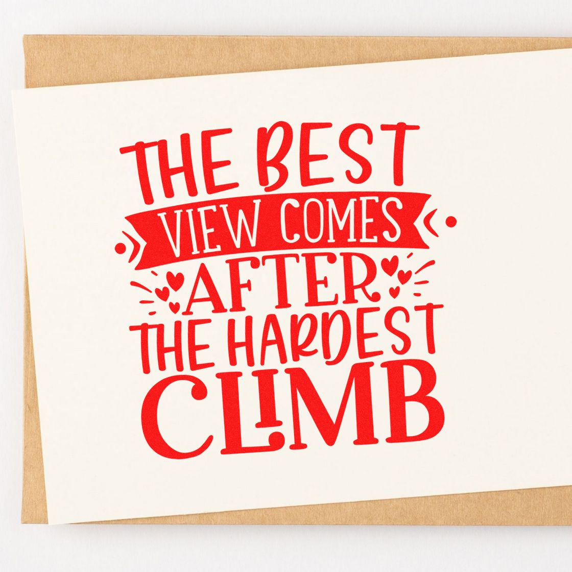 Red decorative rubber stamp seal on cream card with hearts and quote: The best view comes after the hardest climb.
