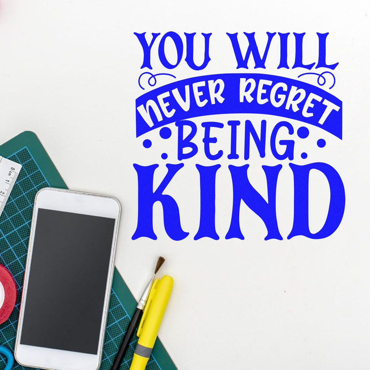 Blue custom stamp/seal quote reading You will never regret being kind beside crafting tools on a white background