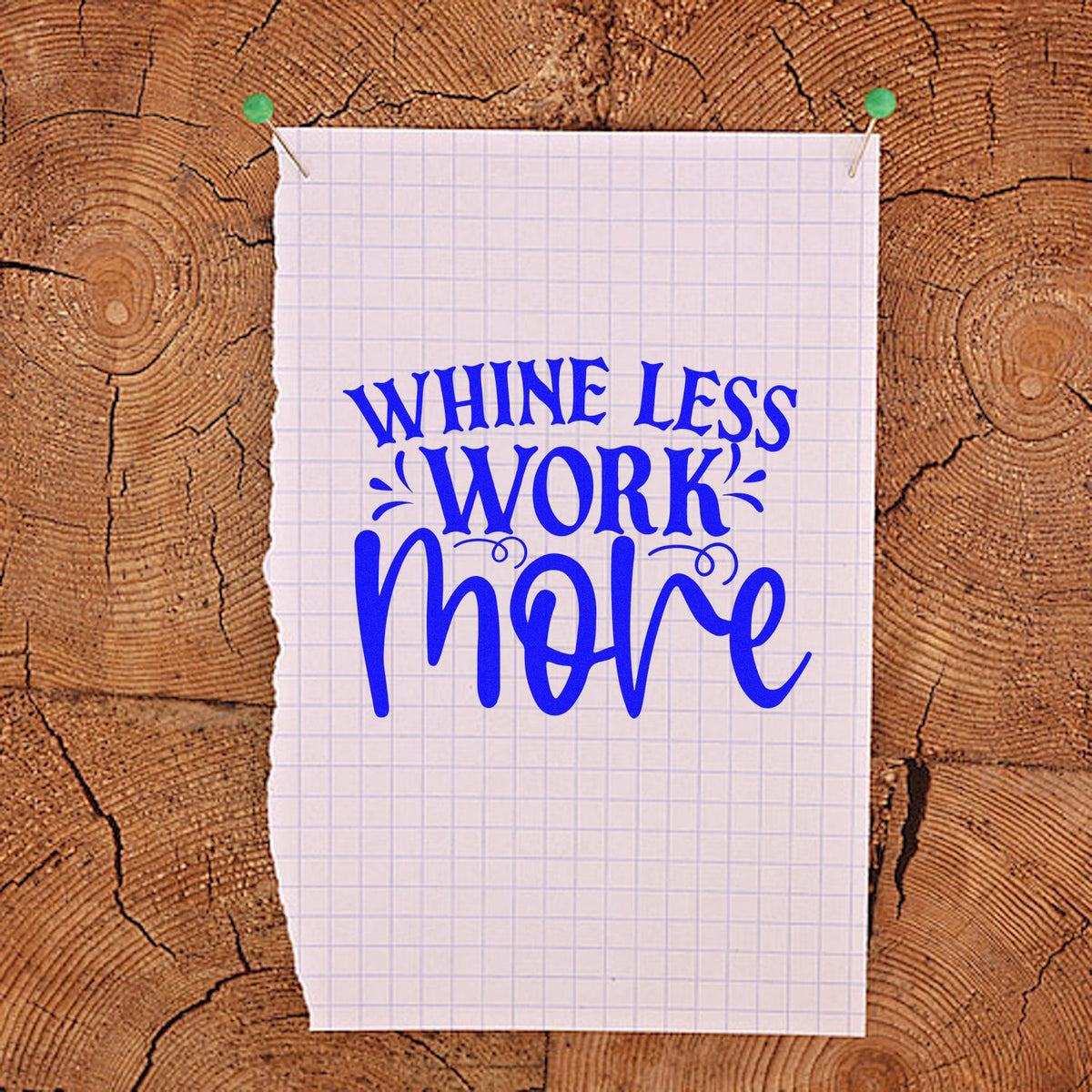 Blue stamp-style Whine Less Work More lettering on white graph paper, pinned with green pushpins against a wood background.