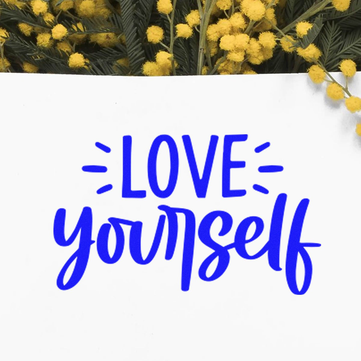 Blue stamp-style LOVE yourself on white seal card, framed by yellow flowers and dark green leaves.