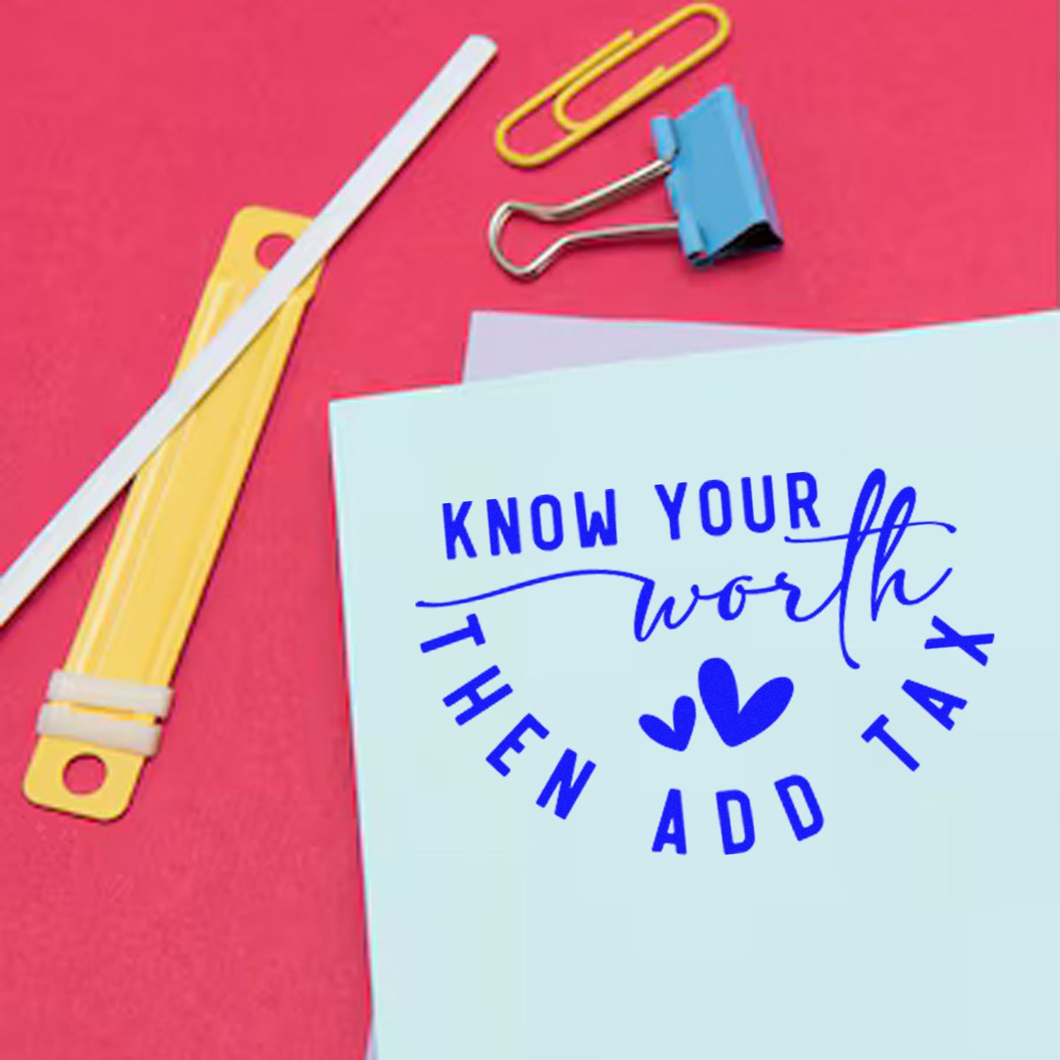 Blue Know Your Worth stamp and seal design with hearts on white paper, beside a yellow label applicator, clips, and pink background.