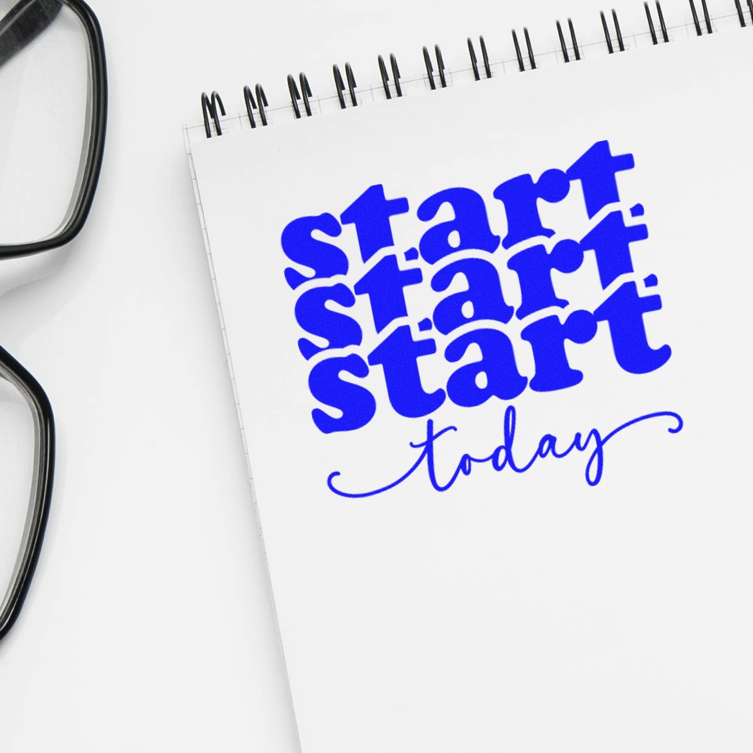 Blue start today stamp/seal on a white spiral notebook, with black eyeglasses at left.