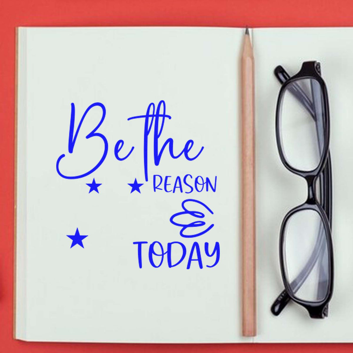 Blue custom stamp and seal reading Be the reason today on a white notebook page, with pencil, black glasses, and a red background.