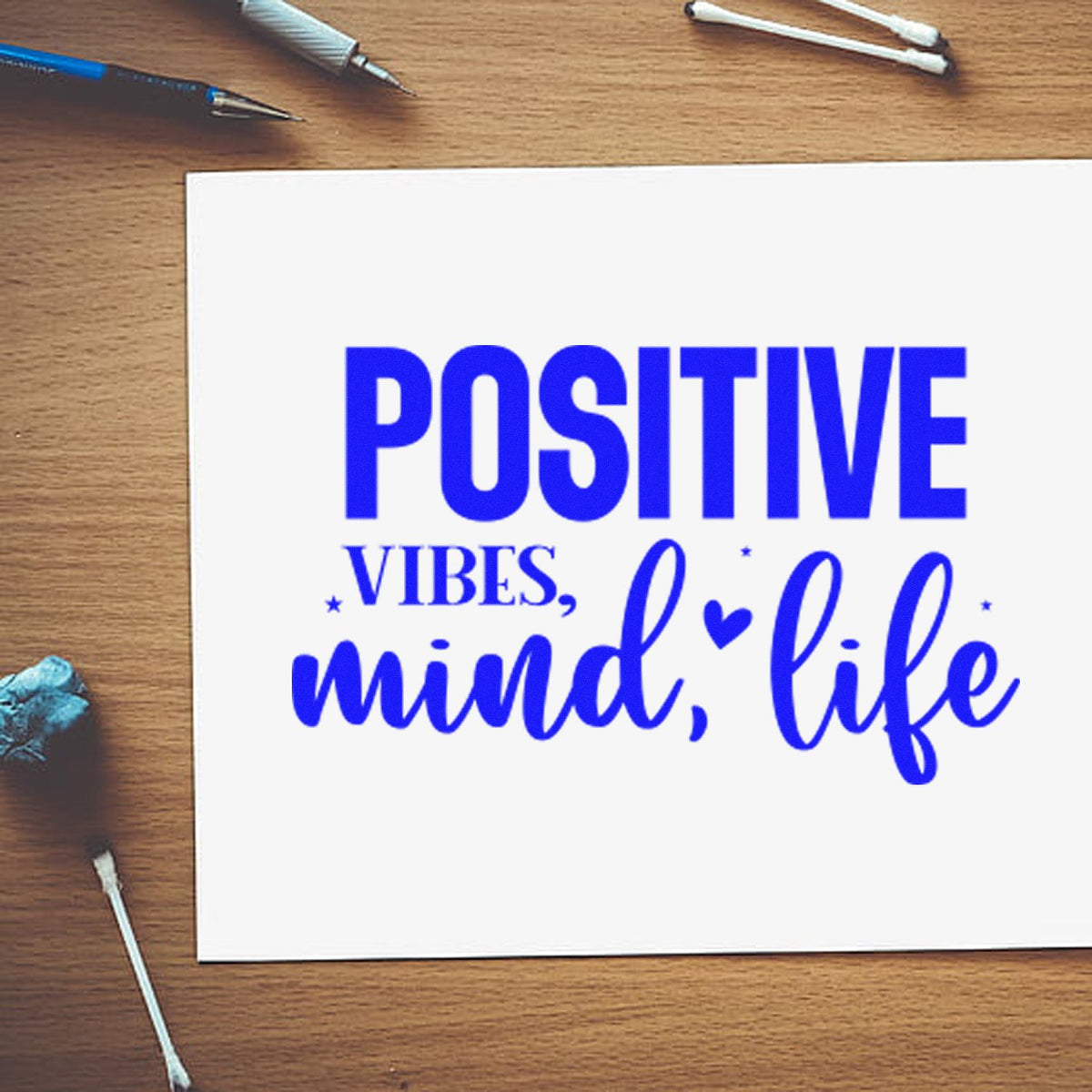 Blue custom stamp and seal reading Positive vibes, mind, life on a white card over a wood desk.