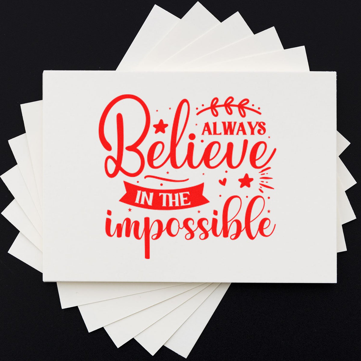 Red motivational stamp on white seal cards reading Believe in the impossible against a black background.