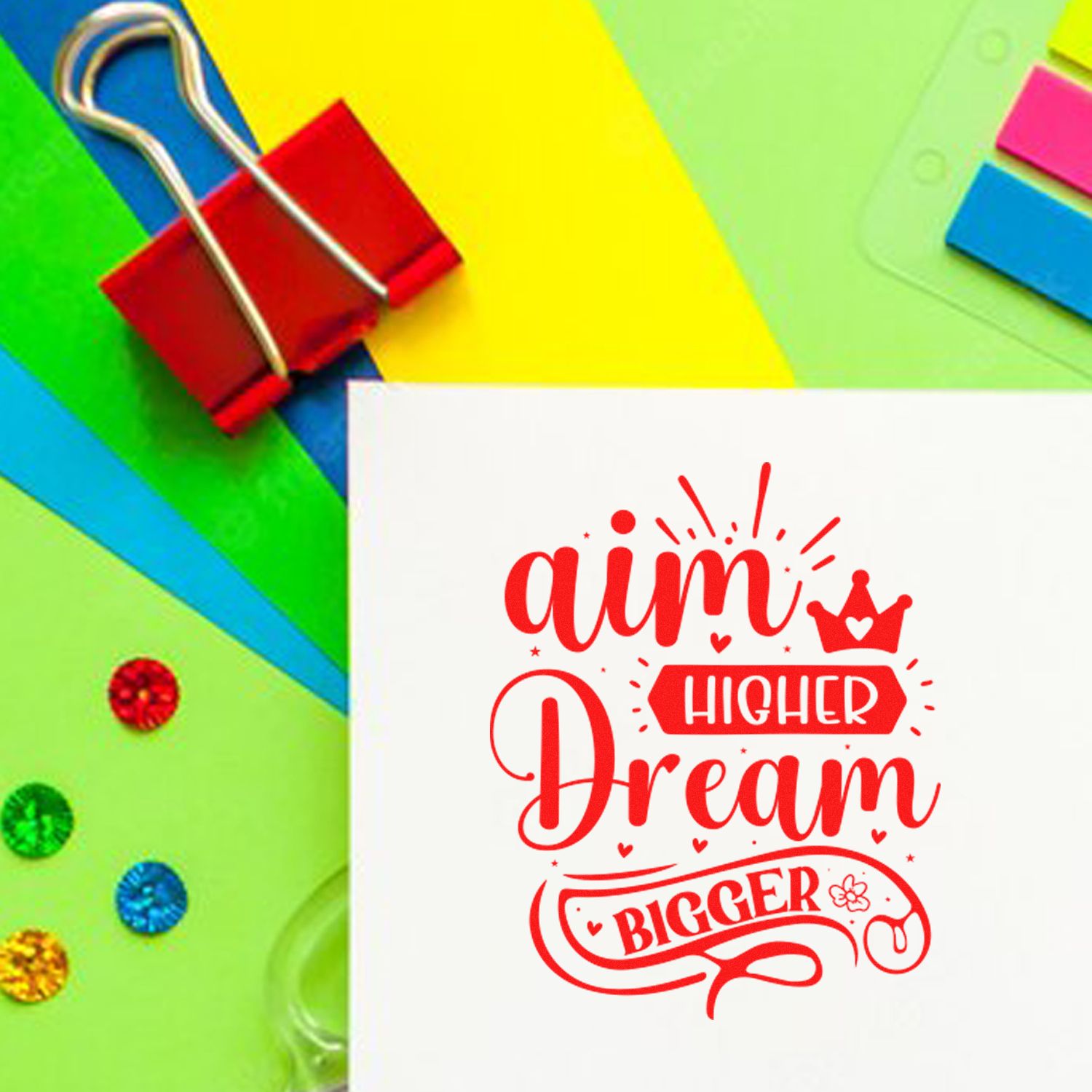 Custom stamp and seal with red Aim Higher Dream Bigger design on white card, set against bright green, yellow and blue stationery.
