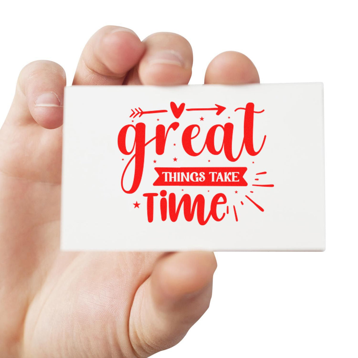 Hand holding a white rubber stamp seal with red great things take time lettering, heart, stars, and arrows.