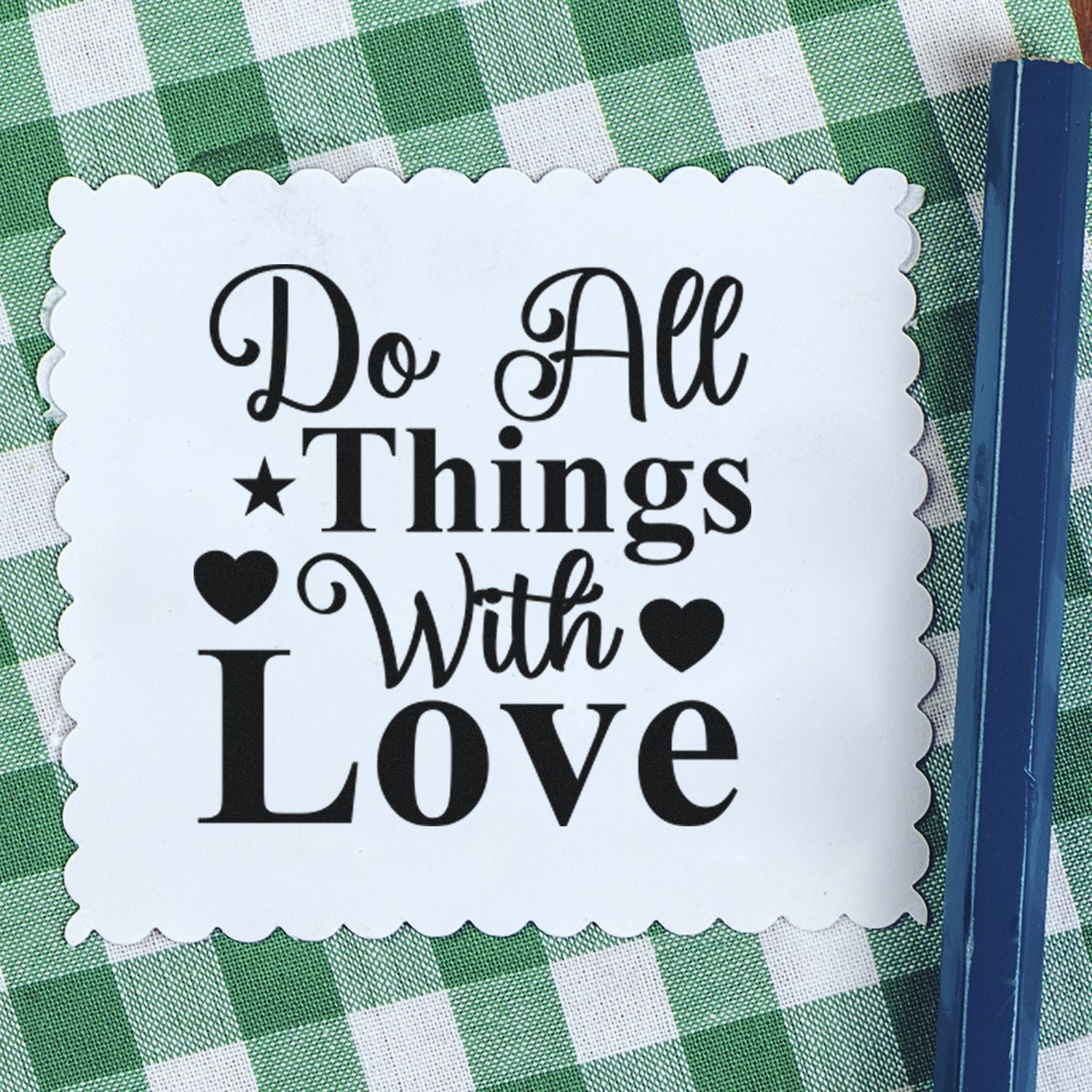 White scalloped stamp seal with black Do All Things With Love text and hearts on green gingham, blue edge.