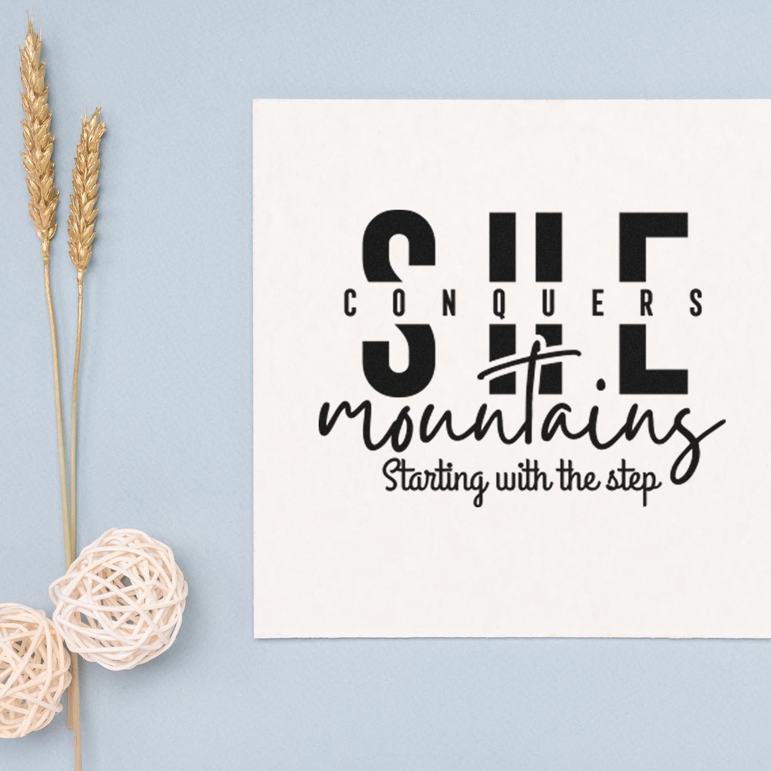 Black custom stamp and seal on white card with Conquers mountains lettering, set on a light blue background.