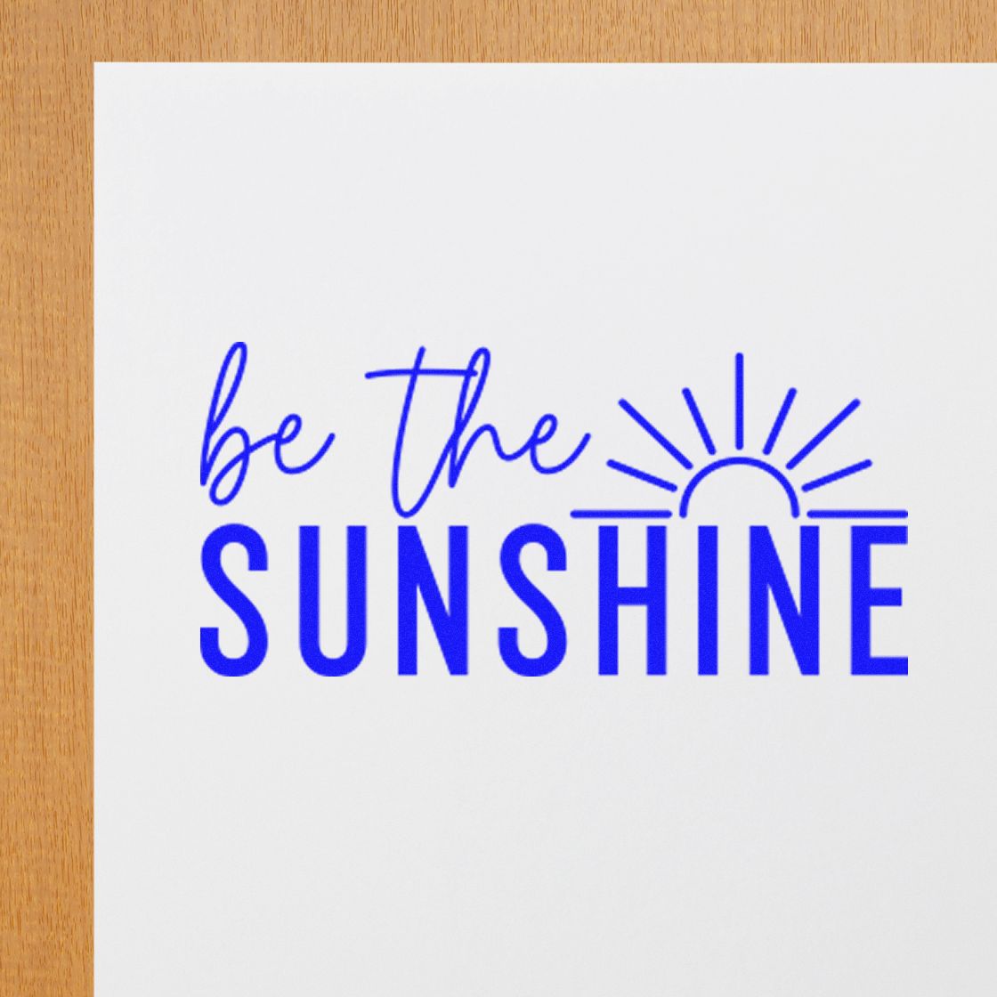 Blue stamp seal reading be the SUNSHINE with a sun icon on white paper, on wood surface