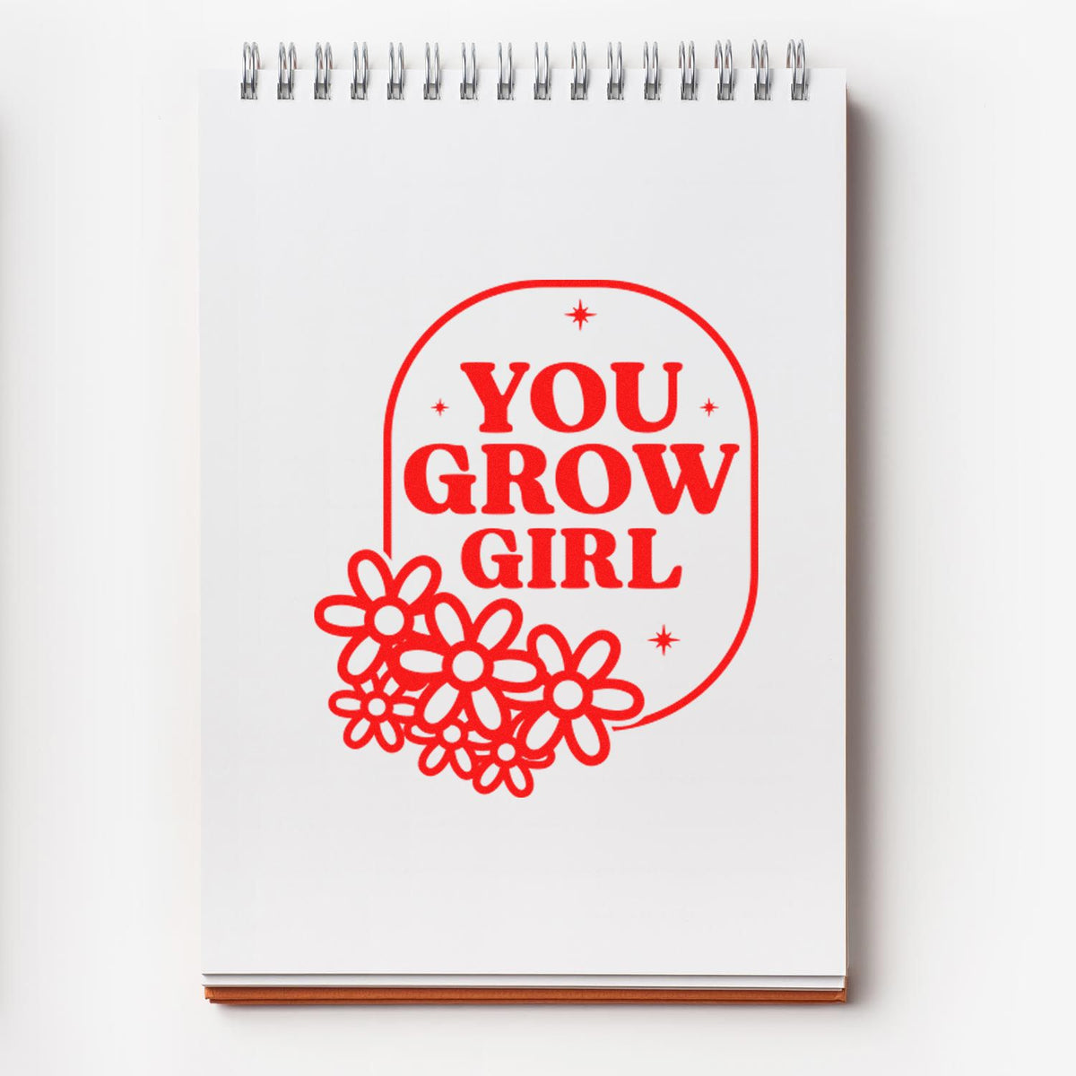 Red You Grow Girl stamp and seal design with floral accents on a white spiral notebook.