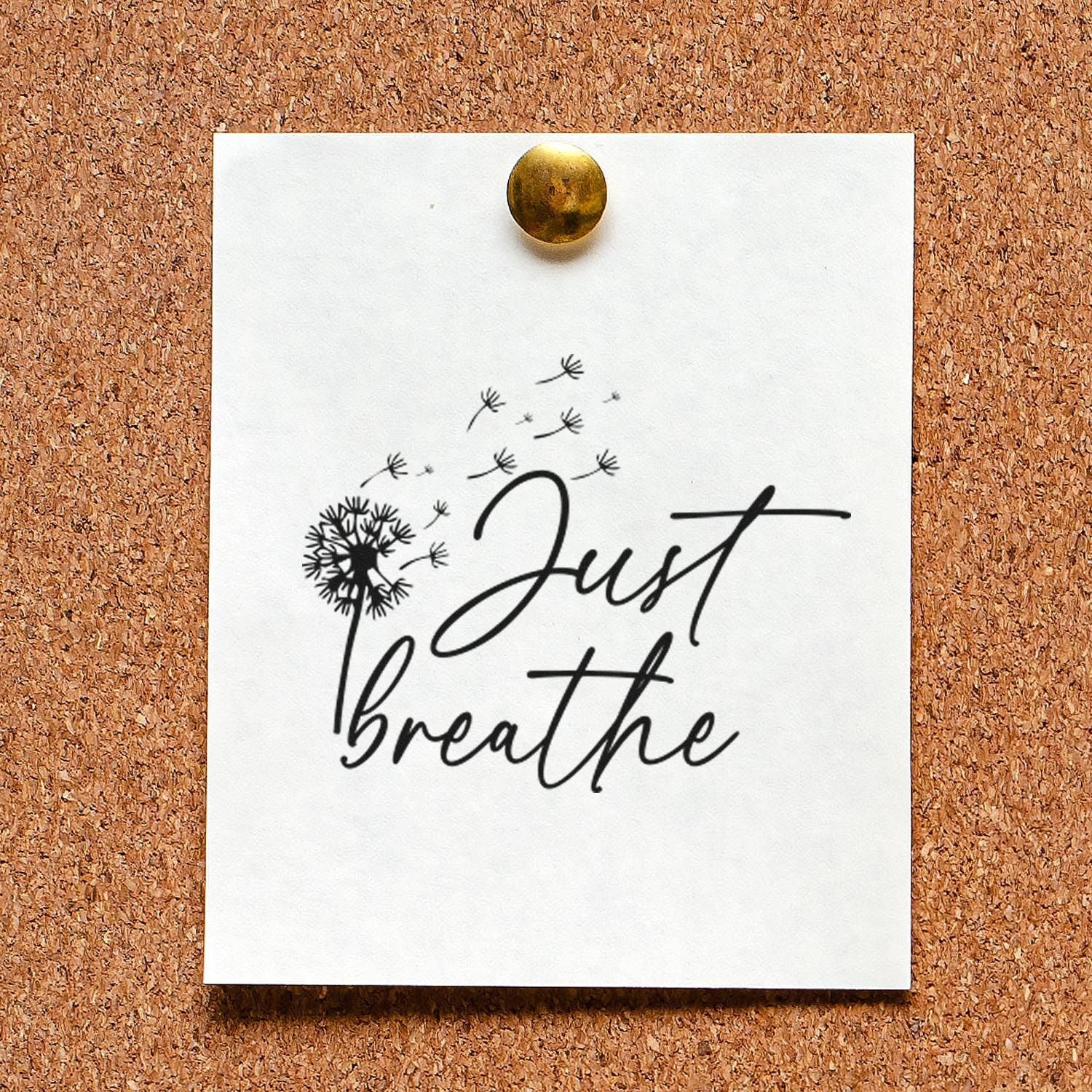White stamp/seal card on corkboard, black Just breathe script with dandelion seeds, pinned by a brass tack.