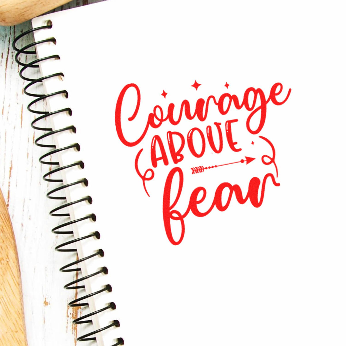 Red Courage Above Fear stamp seal in bright red on white paper, with black spiral binding and small star accents.