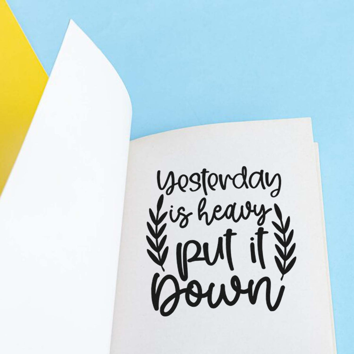 Black stamp seal with Yesterday is heavy, put it down and leaf accents on white paper against light blue and yellow.