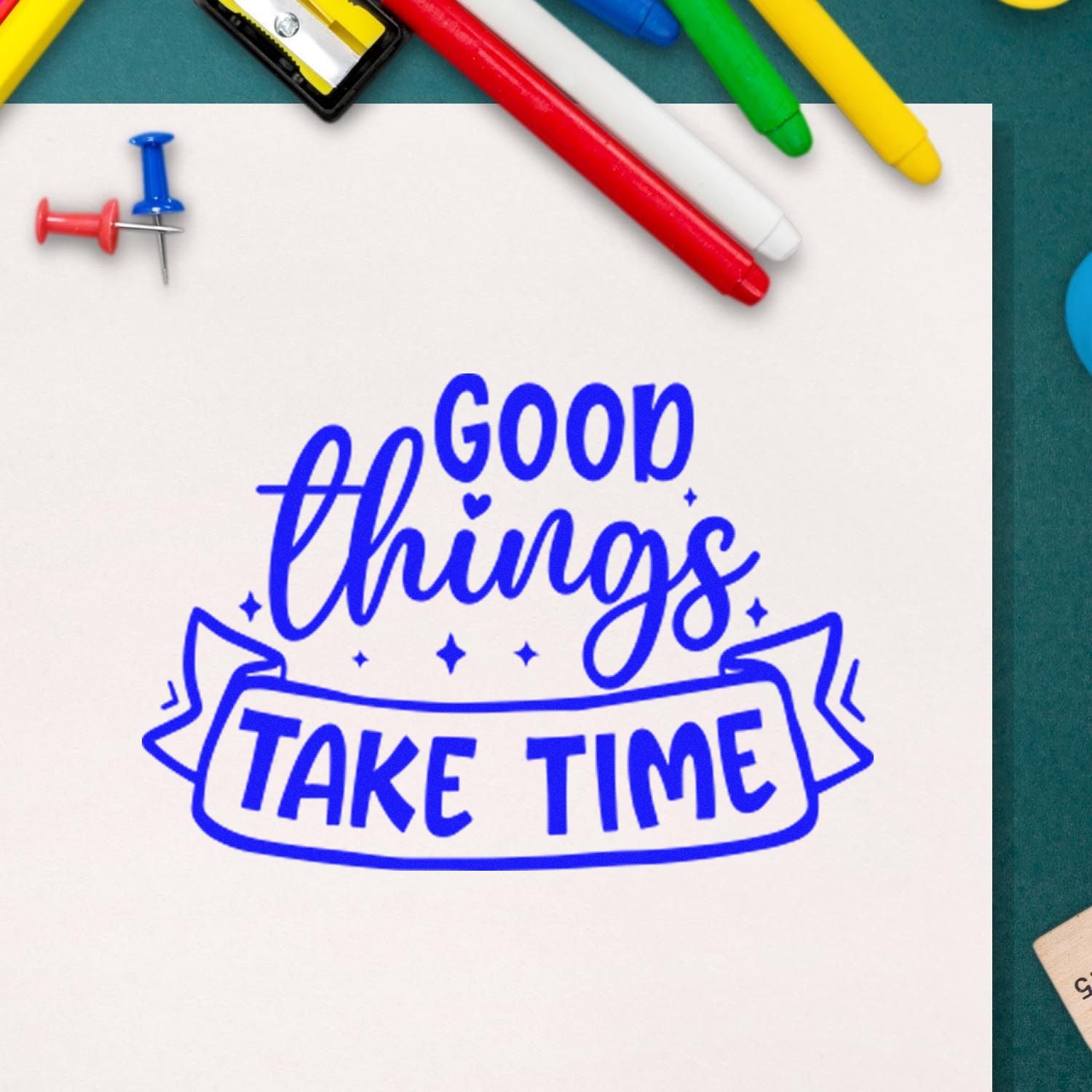 Blue stamp reading Good Things Take Time on white paper, surrounded by colorful stamp and seal tools.