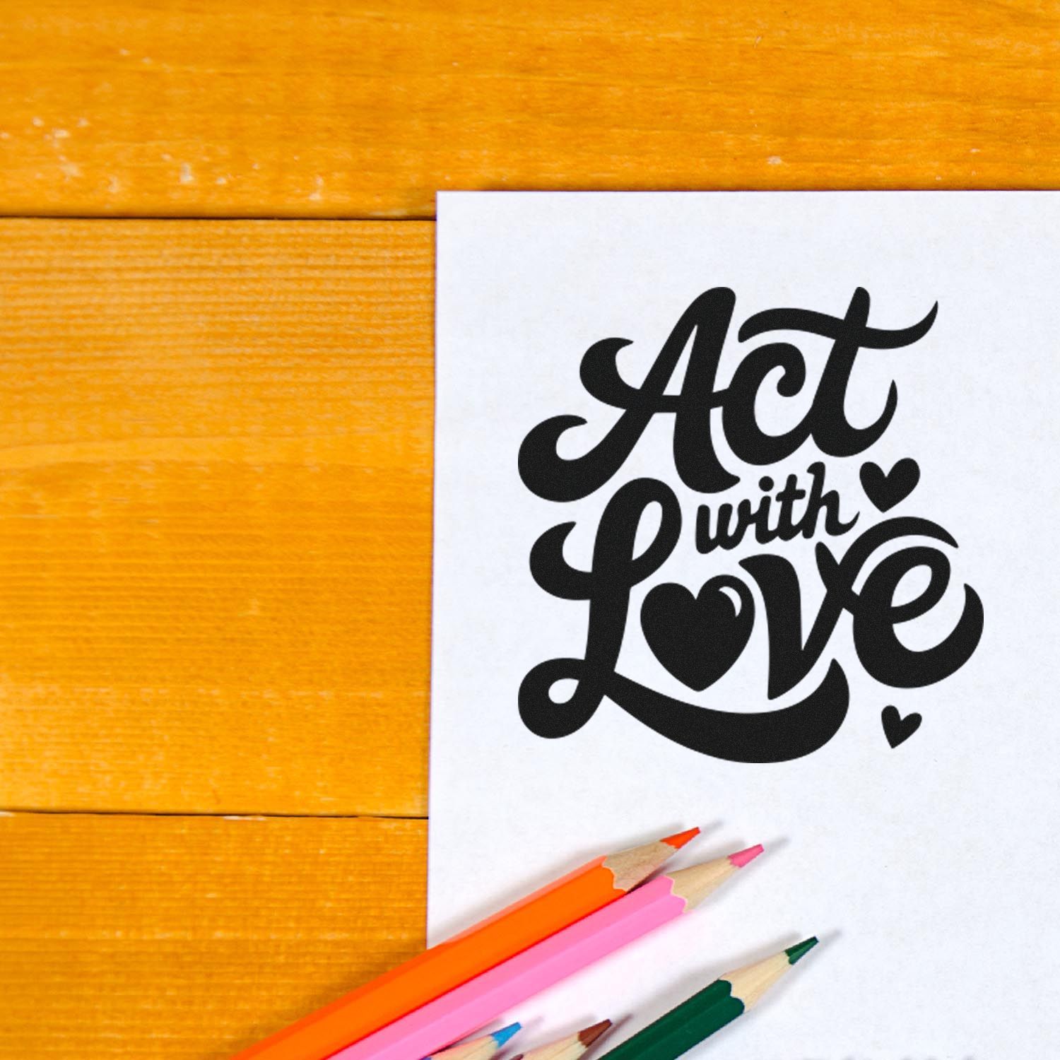 Black Act with Love stamp and seal design on white paper, with hearts and colorful pencils on orange wood
