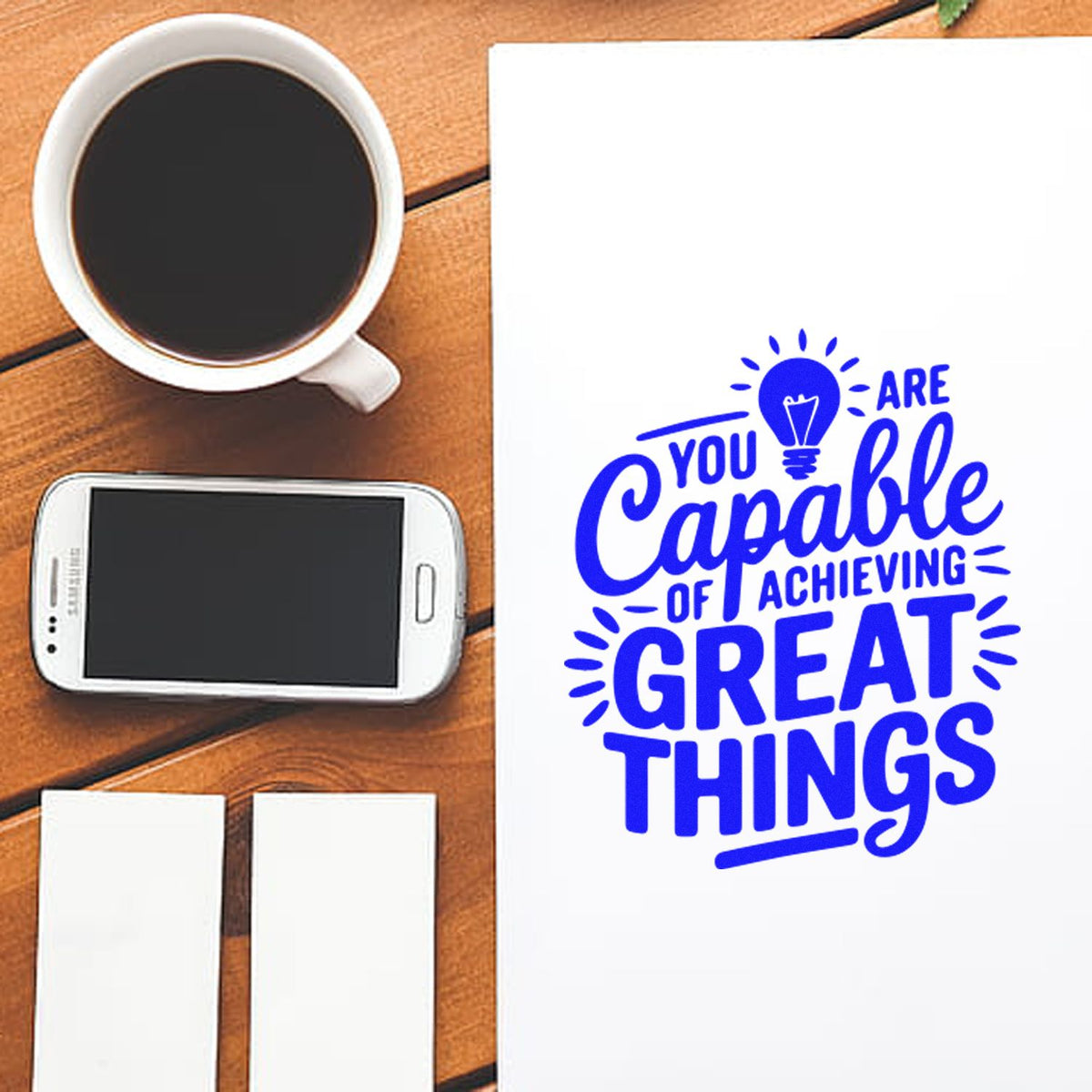 Blue stamp and seal products with motivational quote on white paper, beside coffee, smartphone, and blank white seals on wood desk.