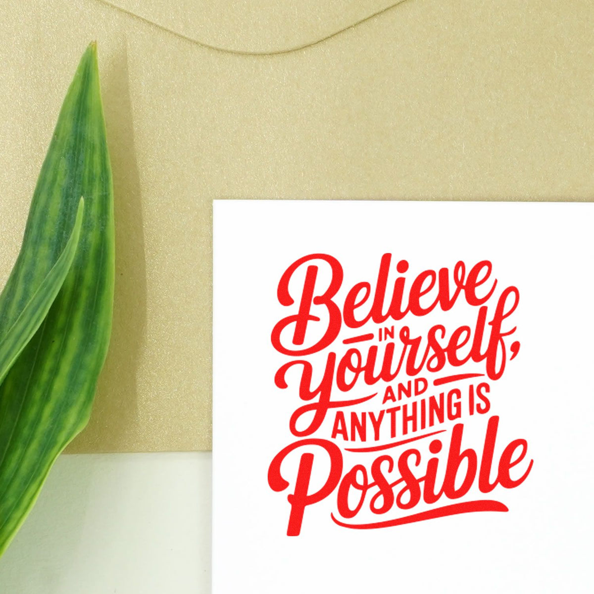 Decorative red rubber stamp and seal reading Believe in yourself and anything is possible on white card, with green leaf.