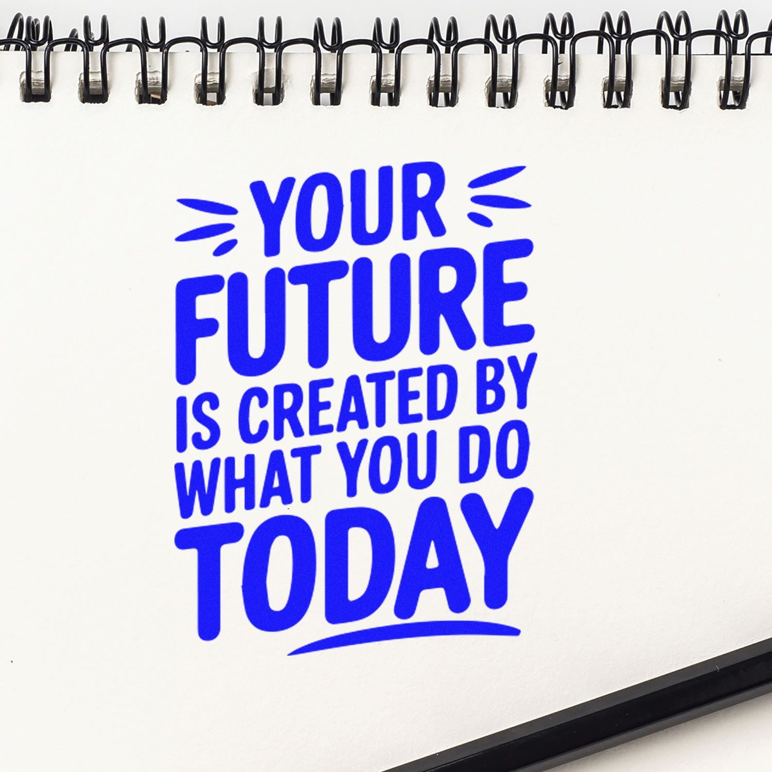 White spiral notebook with bold blue stamp-style seal reading Your future is created by what you do today.