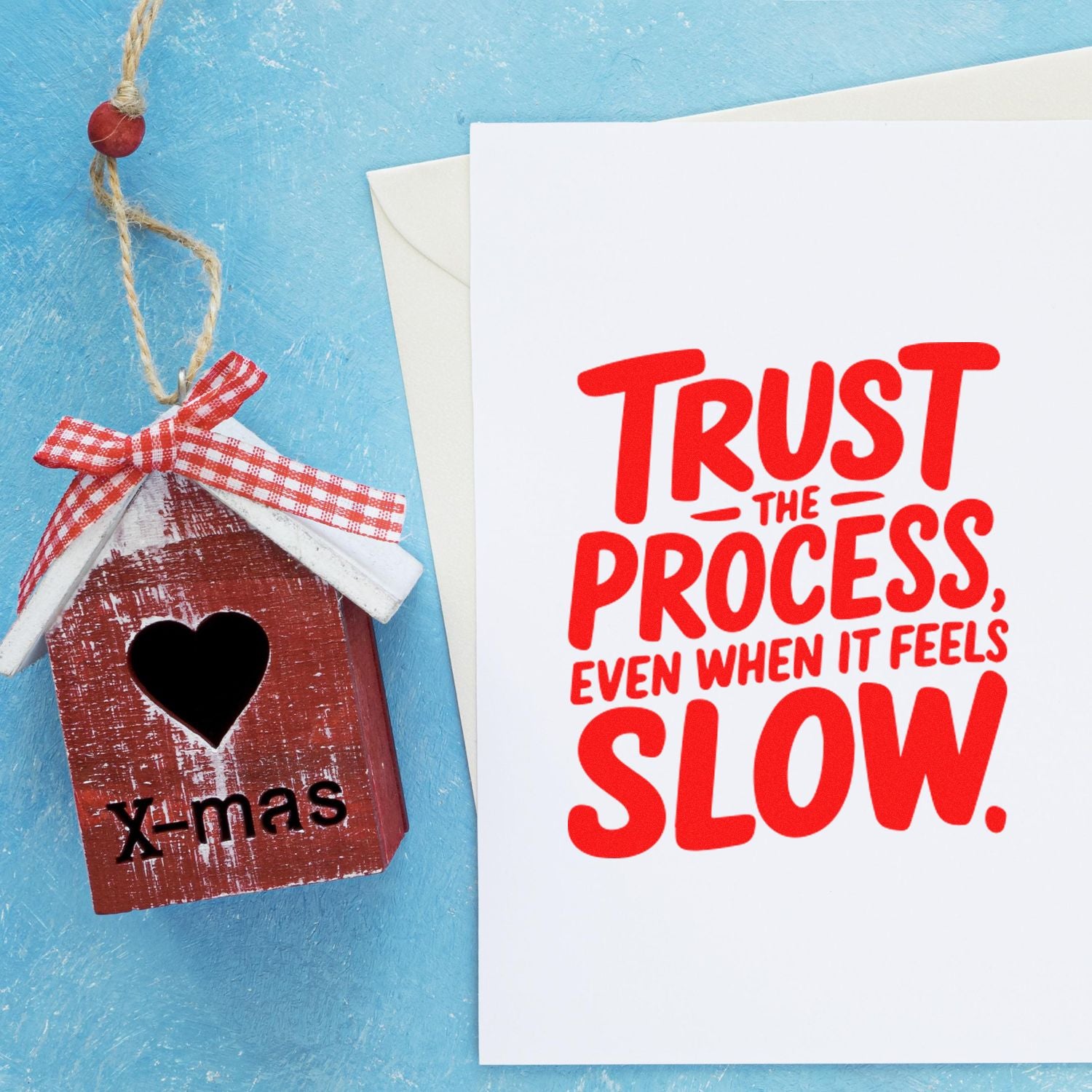 Red birdhouse seal ornament beside a white stamp card with Trust the process, even when it feels slow.