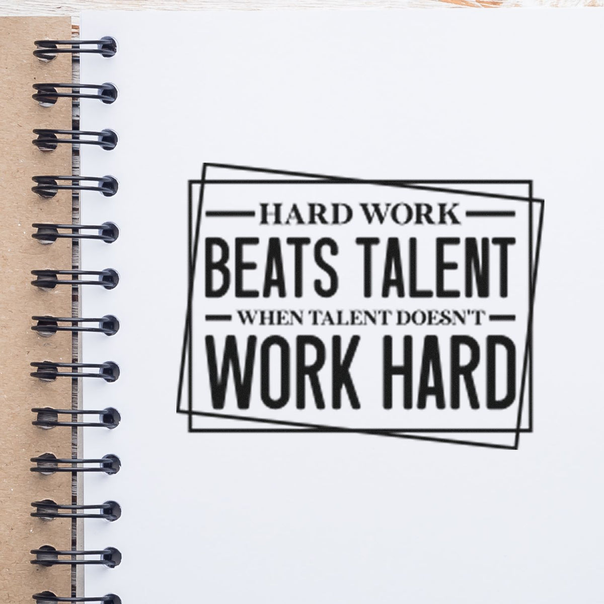 Black motivational stamp seal reading Hard work beats talent when talent doesnt work hard on a white notebook page.