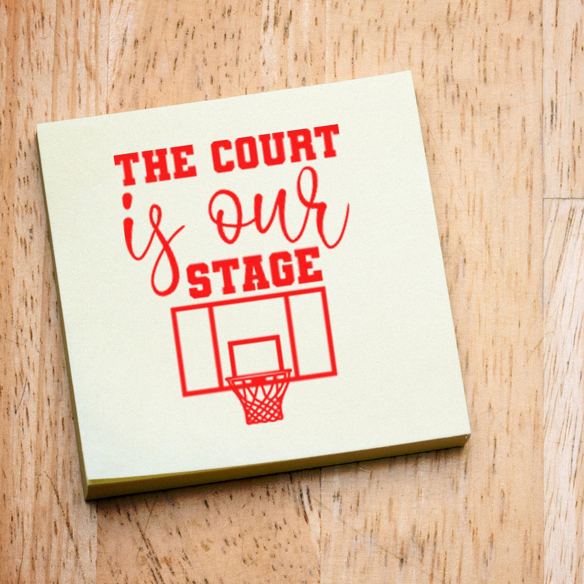 Cream rubber stamp seal with red The Court is Our Stage basketball design on a wood background.