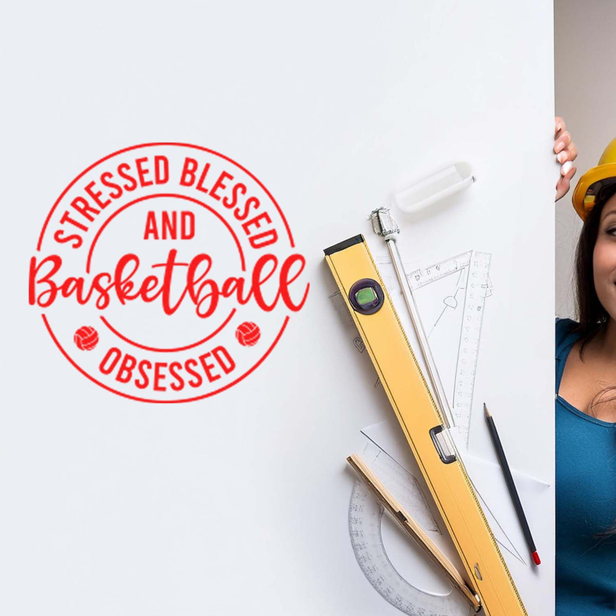 Red basketball-themed stamp seal on white board with yellow level, rulers, pencil, and partial worker in hard hat.