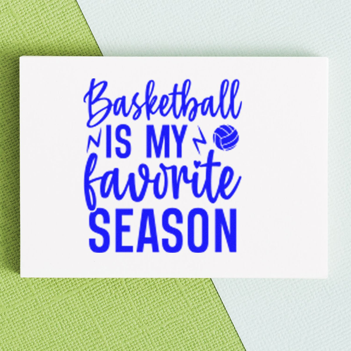 Blue basketball-themed stamp reading Basketball is my favorite season with ball icon on white card over green and white background.