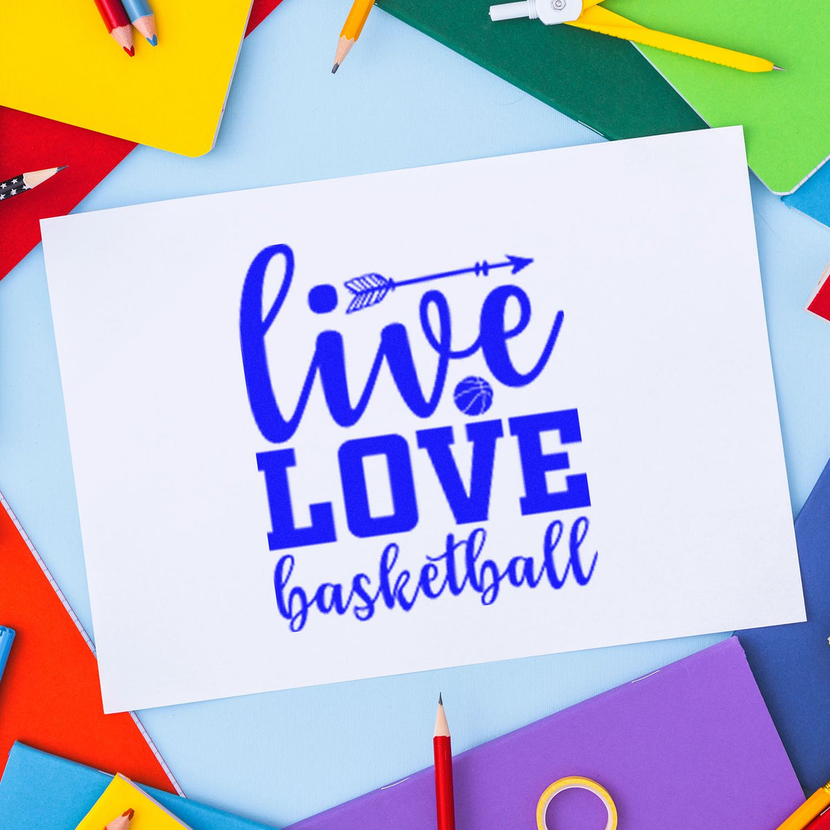 Blue Live Love basketball stamp and seal design on white paper, framed by colorful pencils and notebooks.