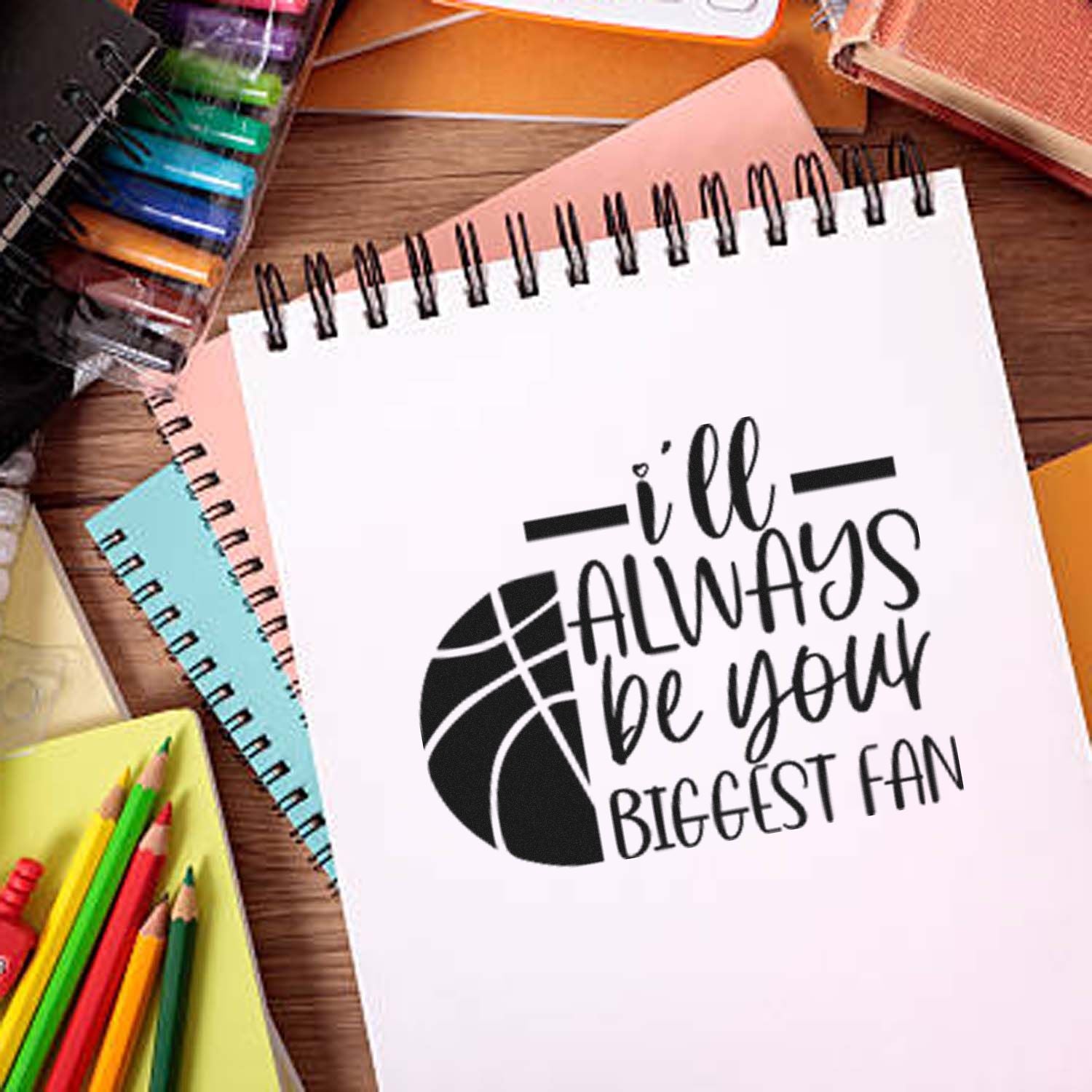Black basketball seal stamp on a white spiral notebook, surrounded by colorful notebooks and pencils.