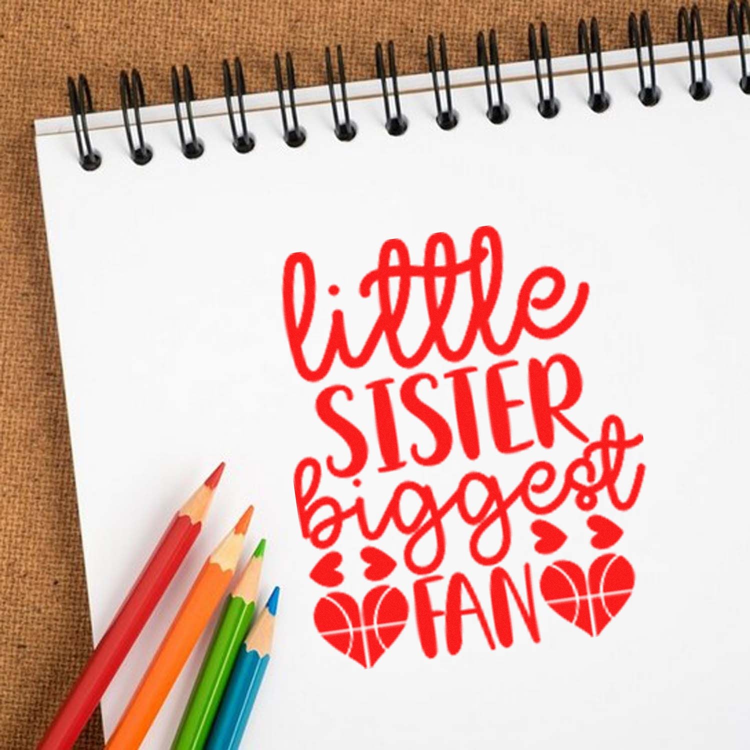 Red little sister bigger fan stamp and seal on white spiral notebook, with heart icons and colorful pencils.