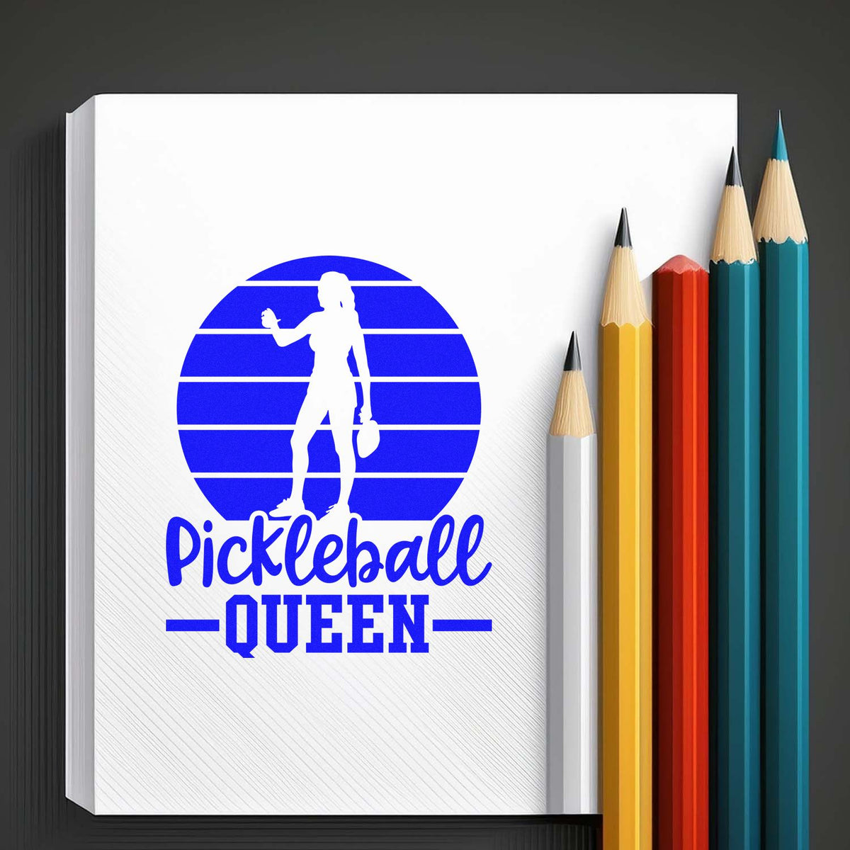 Blue Pickleball Queen stamp and seal design on white pad, with silhouette, striped circle and colorful pencils.