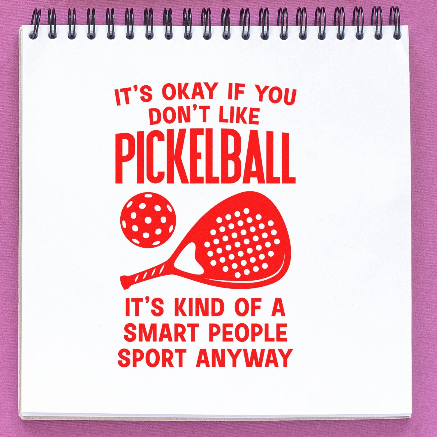 Red pickleball stamp/seal design on white spiral notebook, with paddle and ball graphic and playful slogan.