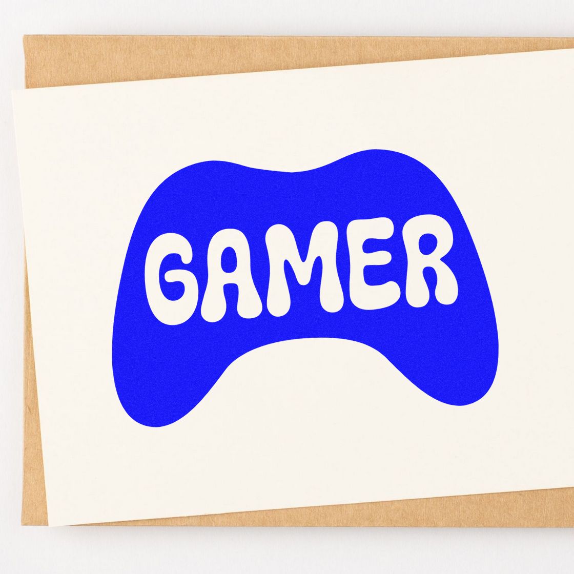 Blue controller-shaped gamer stamp seal with white lettering on a white card over kraft paper.