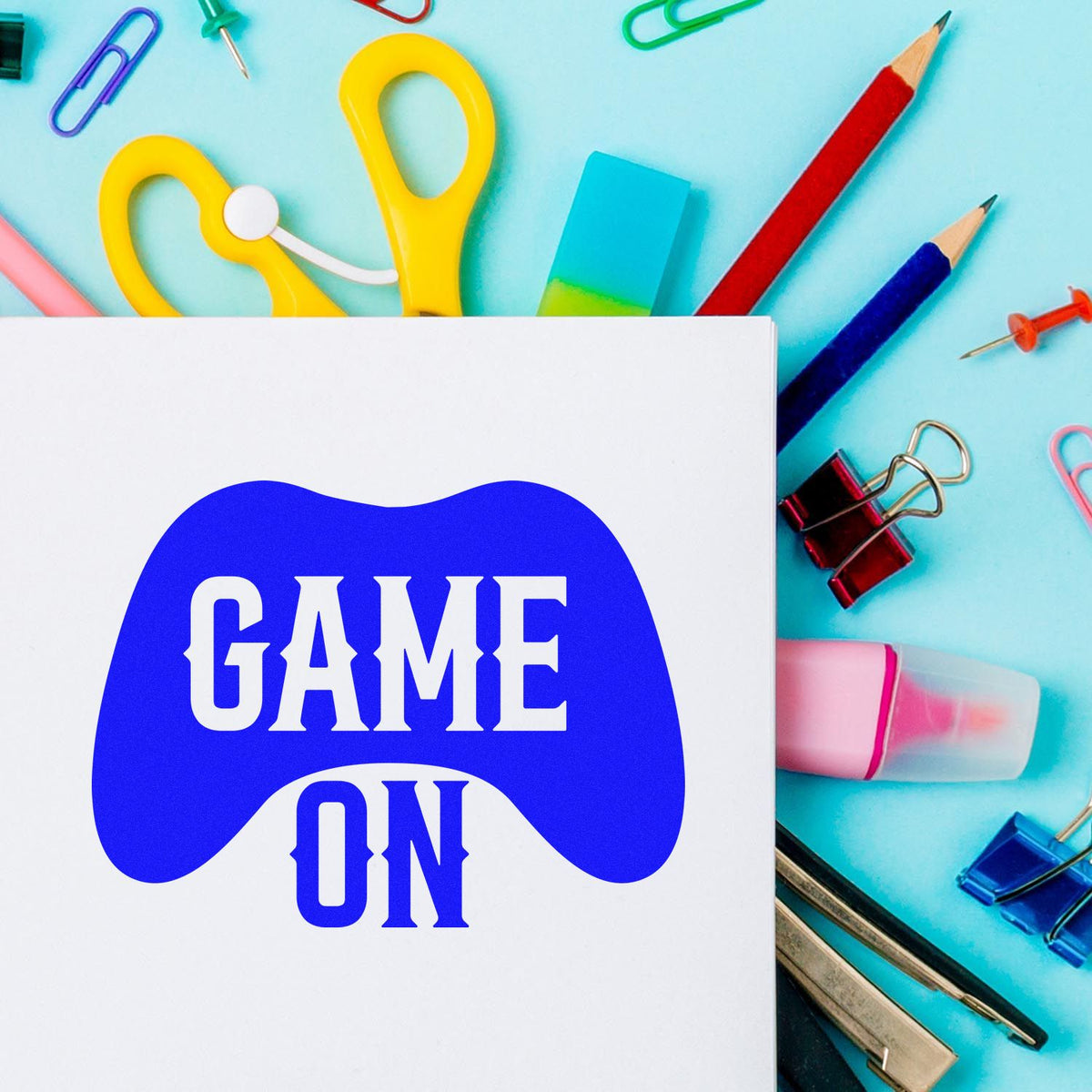 Blue GAME ON gamepad seal on white card, with colorful stamp and seal supplies on a turquoise background.