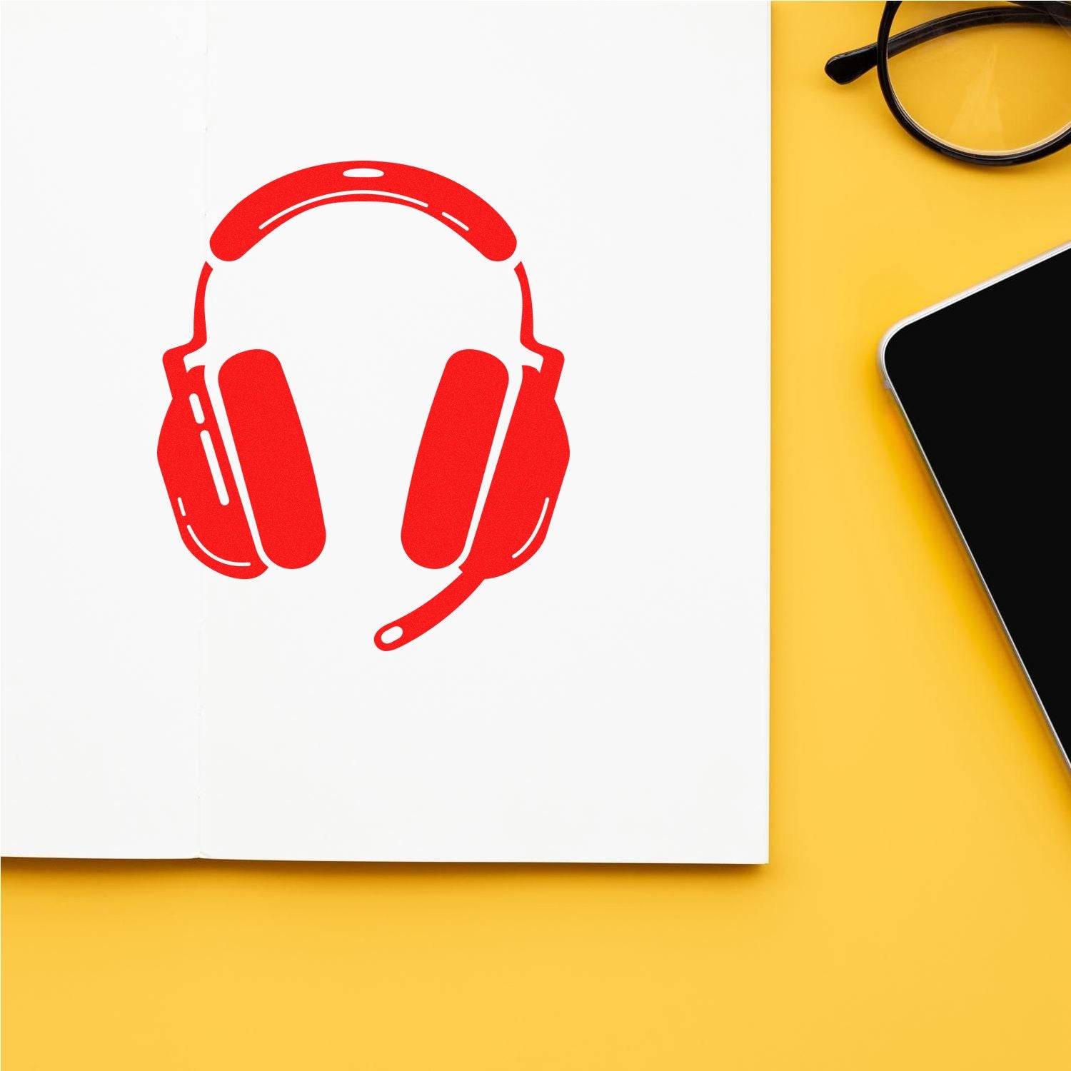 Red headset stamp seal on white notebook, with black glasses and tablet on a yellow background.