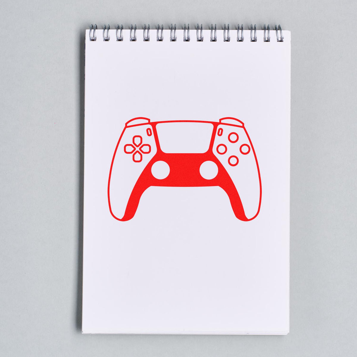 Red game controller stamp and seal design on white spiral notepad, with button icons and cutout details.