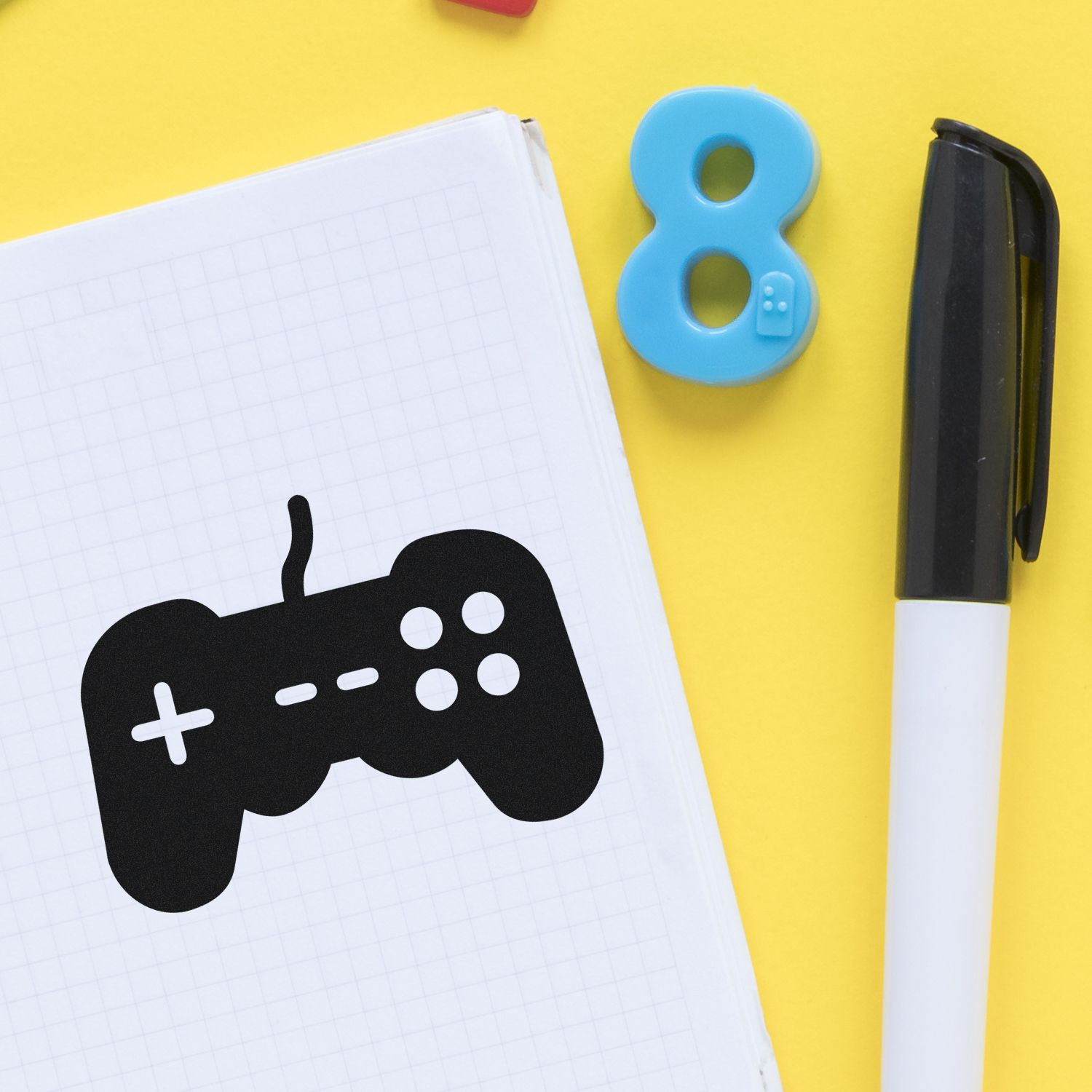 Black game controller stamp on graph notebook, with blue number 8 seal and black marker on bright yellow background.