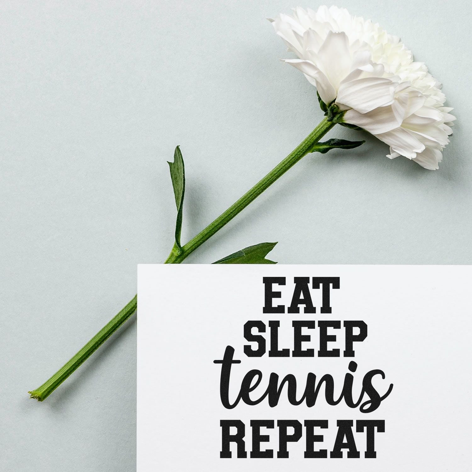 White flower and custom stamp and seal design with black EAT SLEEP tennis REPEAT text on white card, green stem.