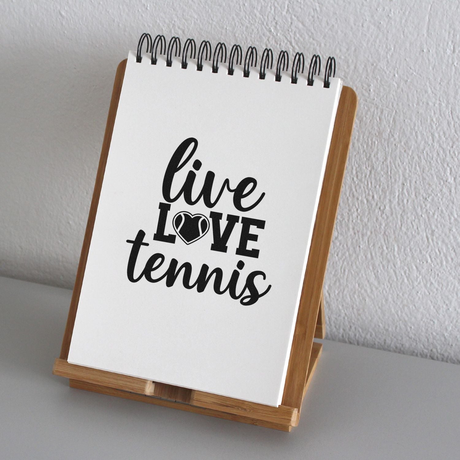 Black live love tennis stamp/seal design on white spiral notepad in bamboo display stand.
