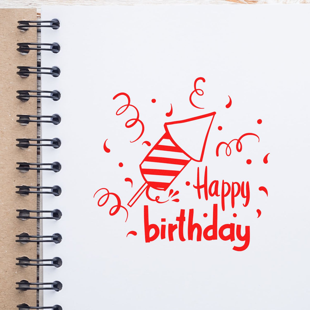 Red Happy Birthday stamp and seal design with party popper and confetti on white spiral notebook.